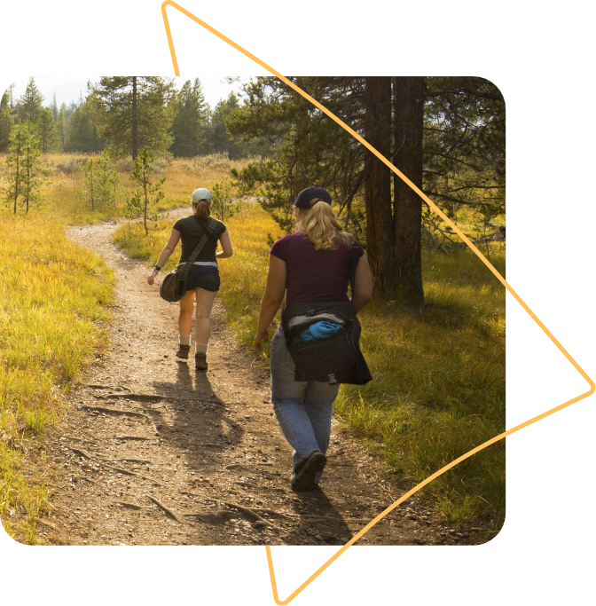 enroll_wyoming_navigator_hero@1x Two women walking down a Wyoming hiking trail. Their backs are to the camera as they walk towards the sunset.